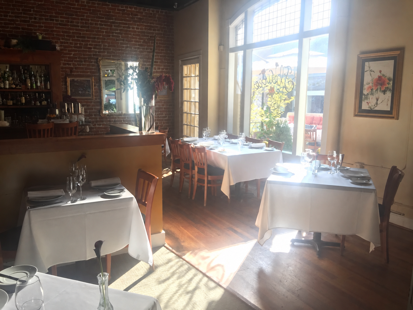 White tablecloths, stemware, and flowers set for dinner beside Fleurie’s front window